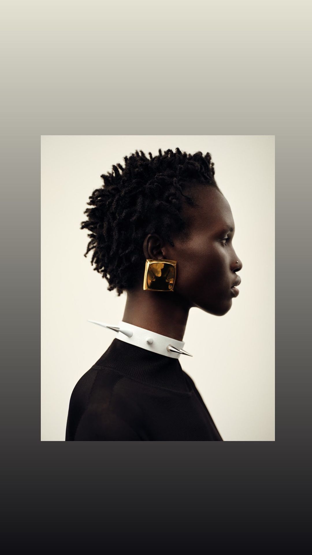 Profile view of Black woman with natural hair, gold square earrings, black top, and spiked white collar against a white backdrop.