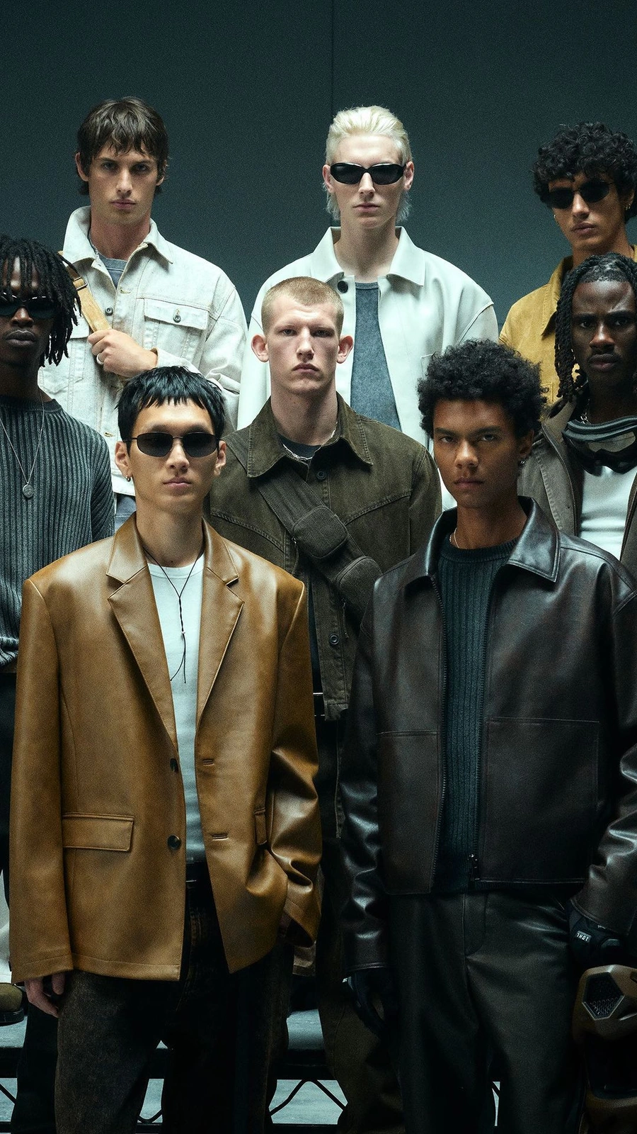 Group of male models in leather jackets and sunglasses posing against a dark grey background by photographer Marc Hibbert