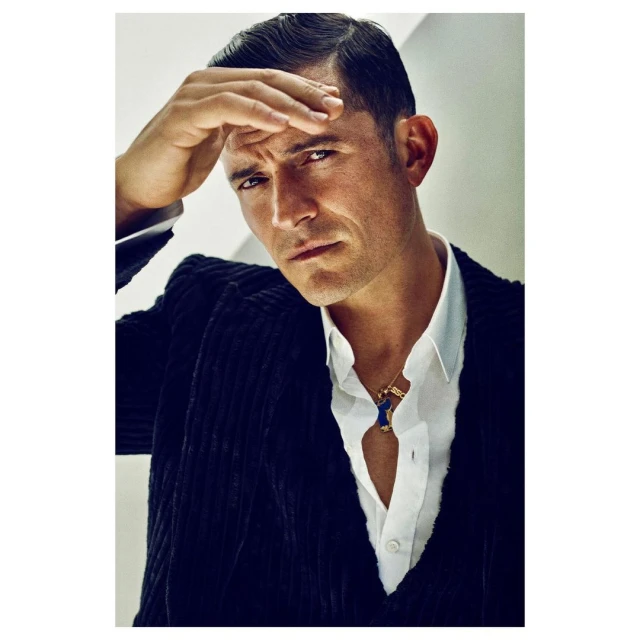 Orlando Bloom portrait in a corduroy suit with a white shirt looking pensively at the camera with hand on his forehead.