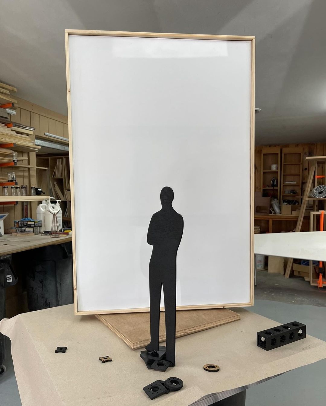 Silhouette of a person standing in front of a large white board surrounded by woodworking tools in a workshop environment.