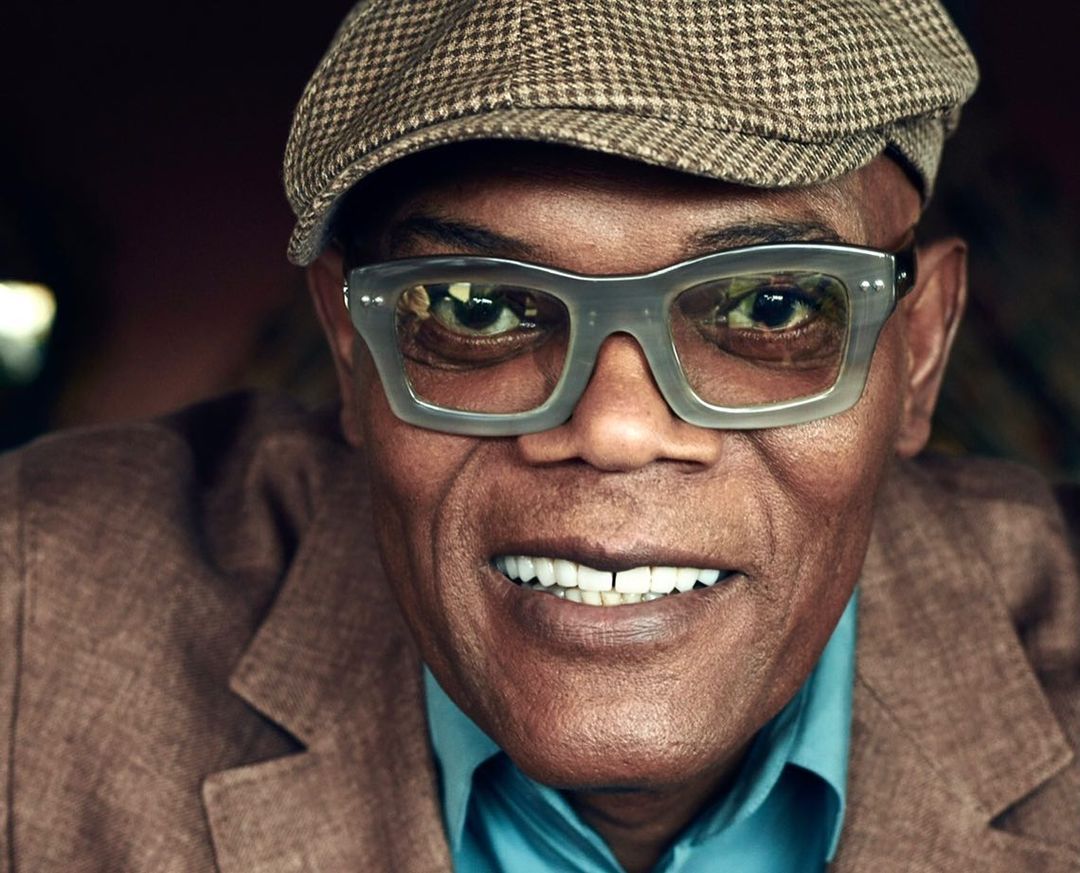 Close-up portrait of smiling African American man wearing a newsboy cap and eyeglasses indoors, showcasing a friendly and stylish look.