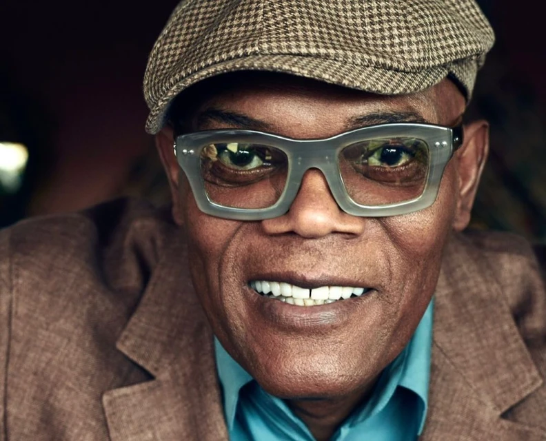 Close-up portrait of smiling African American man wearing a newsboy cap and eyeglasses indoors, showcasing a friendly and stylish look.