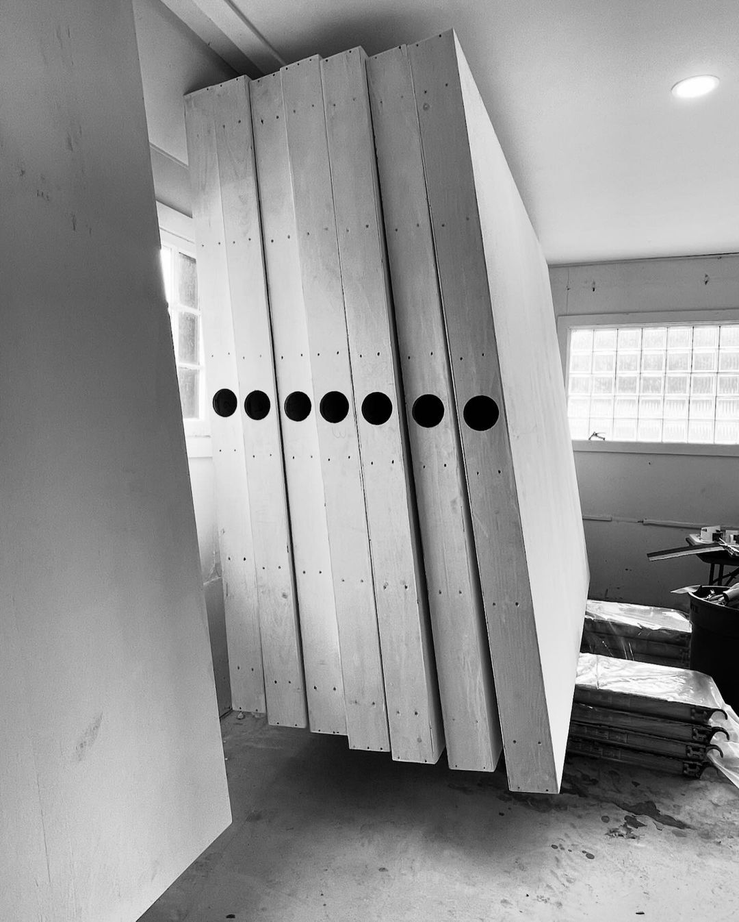Several large rectangular panels with circular holes, leaning against a wall indoors near a window, in a monochromatic grayscale image.