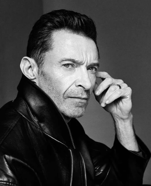 Monochrome portrait of adult male with hand near face, wearing a dark leather jacket, in a photo studio setting with clean background.