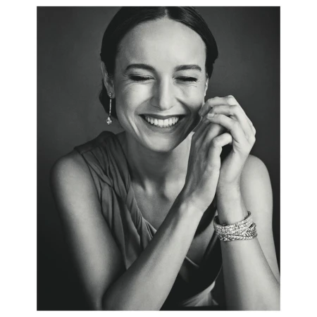 Black and white portrait of a smiling woman with dark hair wearing jewelry. She is indoors against a dark background.