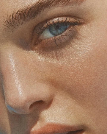 Close-up macro shot of a woman eye and cheek with natural skin texture and warm golden lighting by Marc Philbert