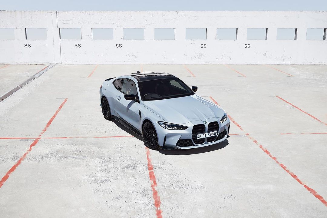Light-blue BMW M4 coupe parked on a concrete surface under bright sunlight, showcasing its design and sporty features.