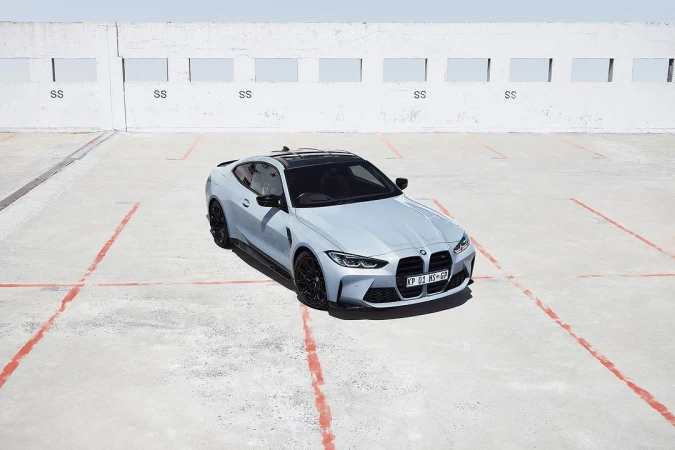 Light-blue BMW M4 coupe parked on a concrete surface under bright sunlight, showcasing its design and sporty features.