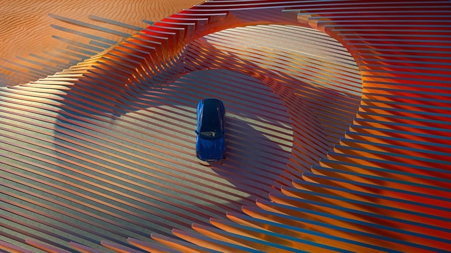 Aerial view of a blue car driving on a geometric, orange and gray surface with a desert background, showcasing automotive design.