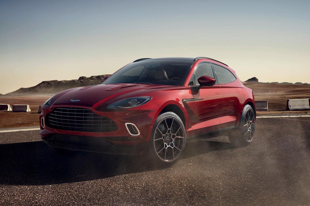 Red Aston Martin DBX SUV on paved desert road under clear sky, showcasing automotive design, luxury vehicle, and performance capabilities.