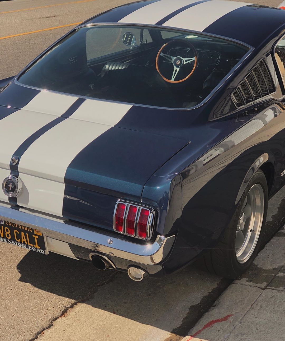 Rear quarter view of a blue and white striped classic Ford Mustang parked on a city street, showcasing its iconic design.
