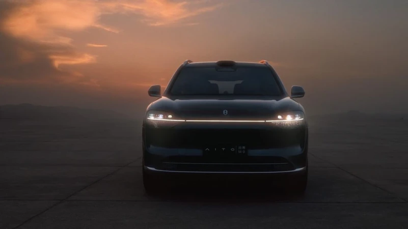 Front view of a dark AITO SUV with headlights illuminated against a dusky sky at sunset. The car is parked on a dark surface.