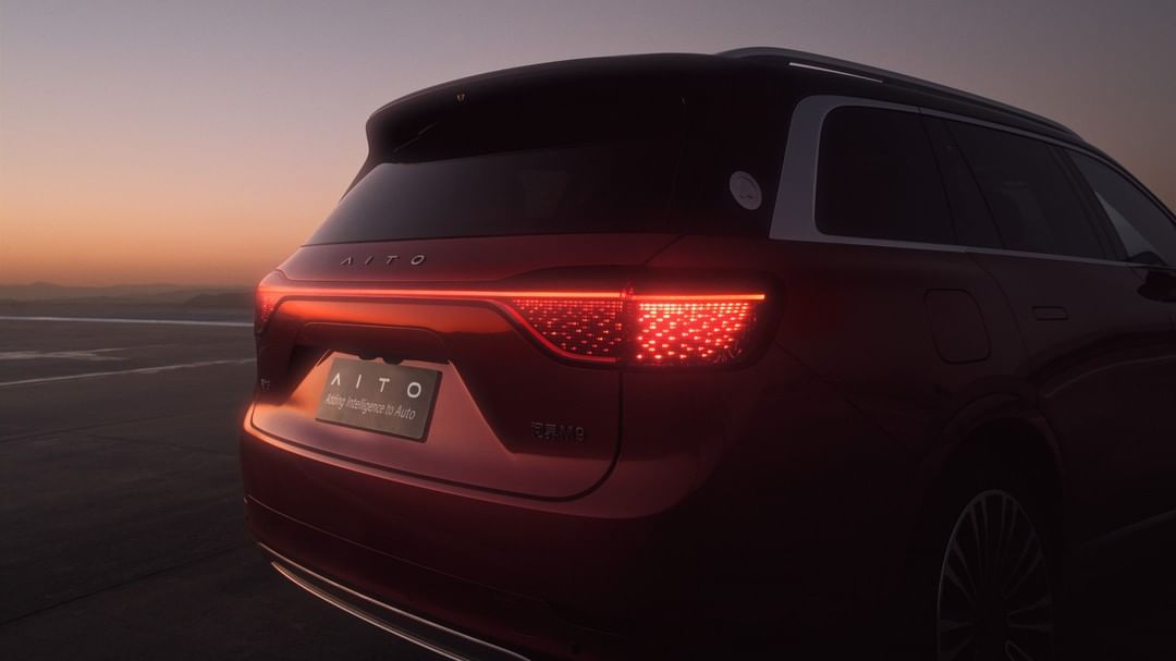 Rear view of a red AITO SUV with illuminated tail lights, parked on an open lot against an evening sky at dusk.