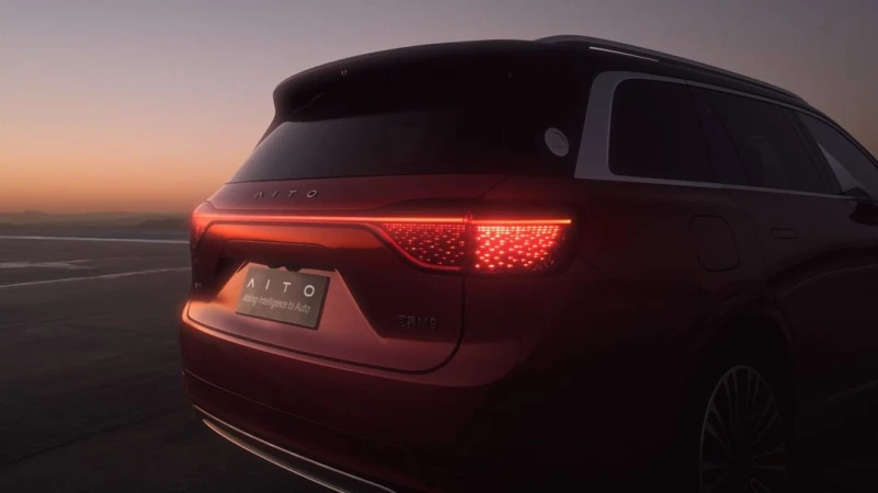 Rear view of a red AITO SUV with illuminated tail lights, parked on an open lot against an evening sky at dusk.
