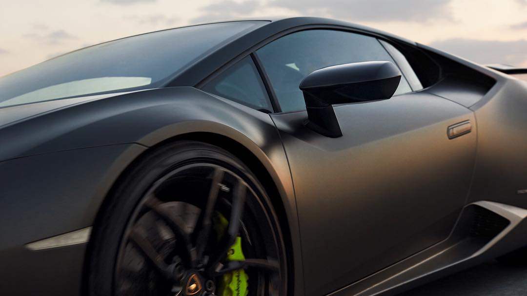 Low angle view of a matte gray Lamborghini Huracan with black rims and bright yellow calipers against a cloudy sky at dusk.