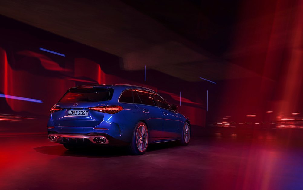 Rear view of a blue Mercedes-Benz C43 AMG wagon in motion, showcasing sleek design, quad exhausts, and red and blue lighting.