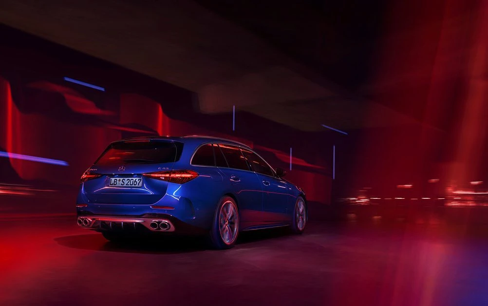 Rear view of a blue Mercedes-Benz C43 AMG wagon in motion, showcasing sleek design, quad exhausts, and red and blue lighting.