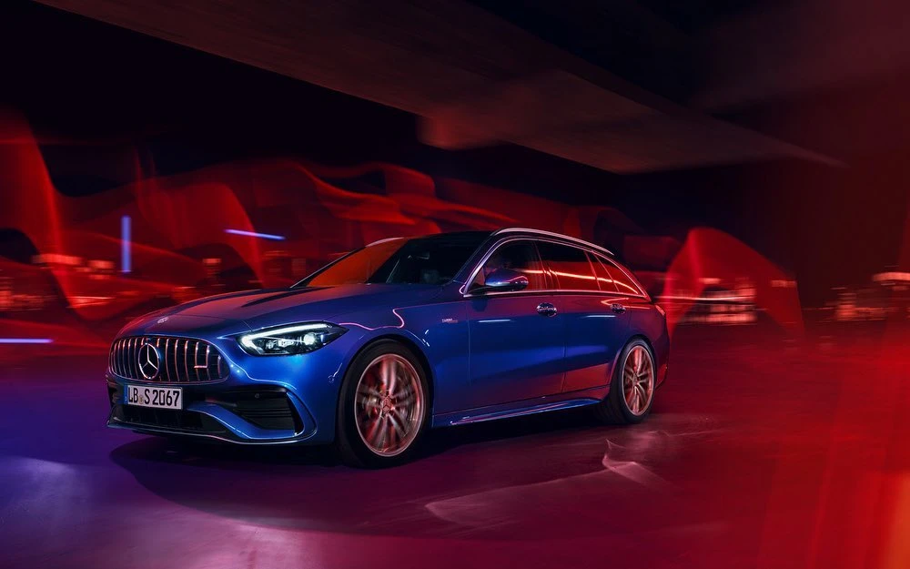 A blue Mercedes-Benz station wagon is shown at eye-level, illuminated by red and purple light in a darkened environment, creating motion blur.