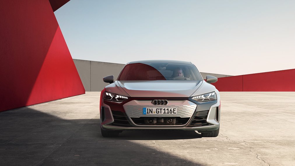 Sleek silver Audi e-tron GT 116e electric car front view with signature grill, headlights, parked on a concrete surface in an urban environment.