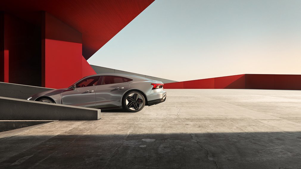Sleek silver Audi e-tron GT parked inside a modern concrete structure with striking red architectural accents and ample copy space.