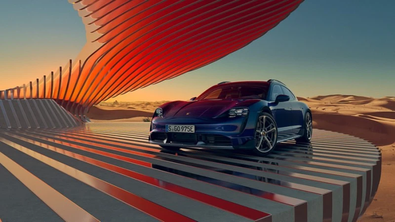 Sleek blue Porsche Taycan Cross Turismo electric car displayed on a striped platform against a desert backdrop with a red sculpture.