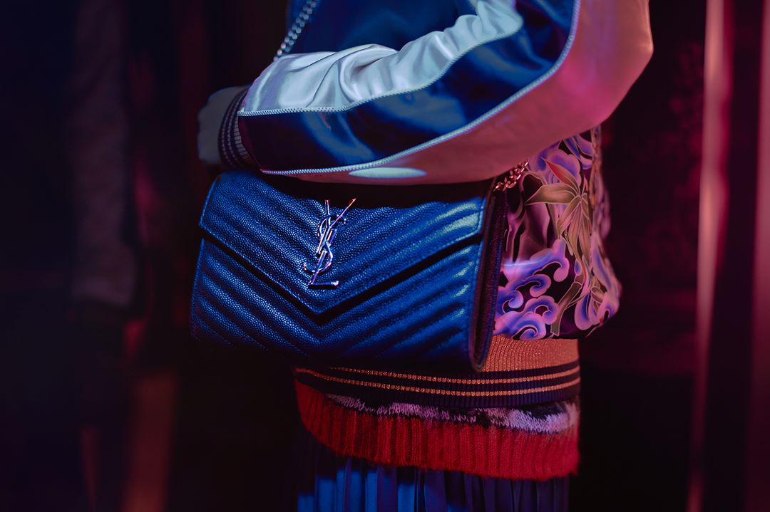Close-up of a blue chevron quilted leather YSL shoulder bag with silver hardware, worn with a printed jacket and colorful skirt.