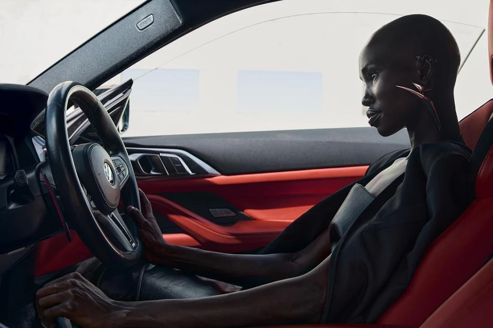 Woman in driver's seat of red BMW car. Close-up portrait view of female looking straight. Automotive fashion and lifestyle content.
