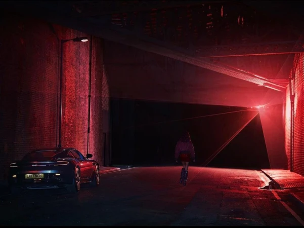 A blue sports car parked in a brick tunnel with a person on roller skates illuminated in red light in the distance.