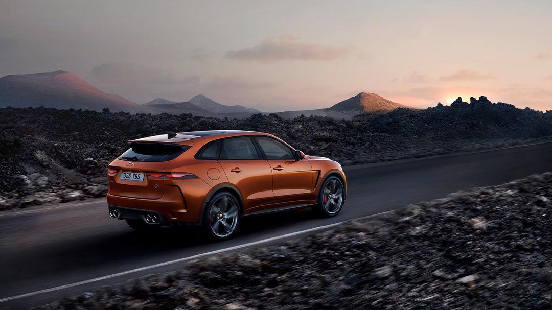 Copper-colored Jaguar F-Pace SVR driving on a desert road with distant mountains in the background at sunset. Automotive photography.