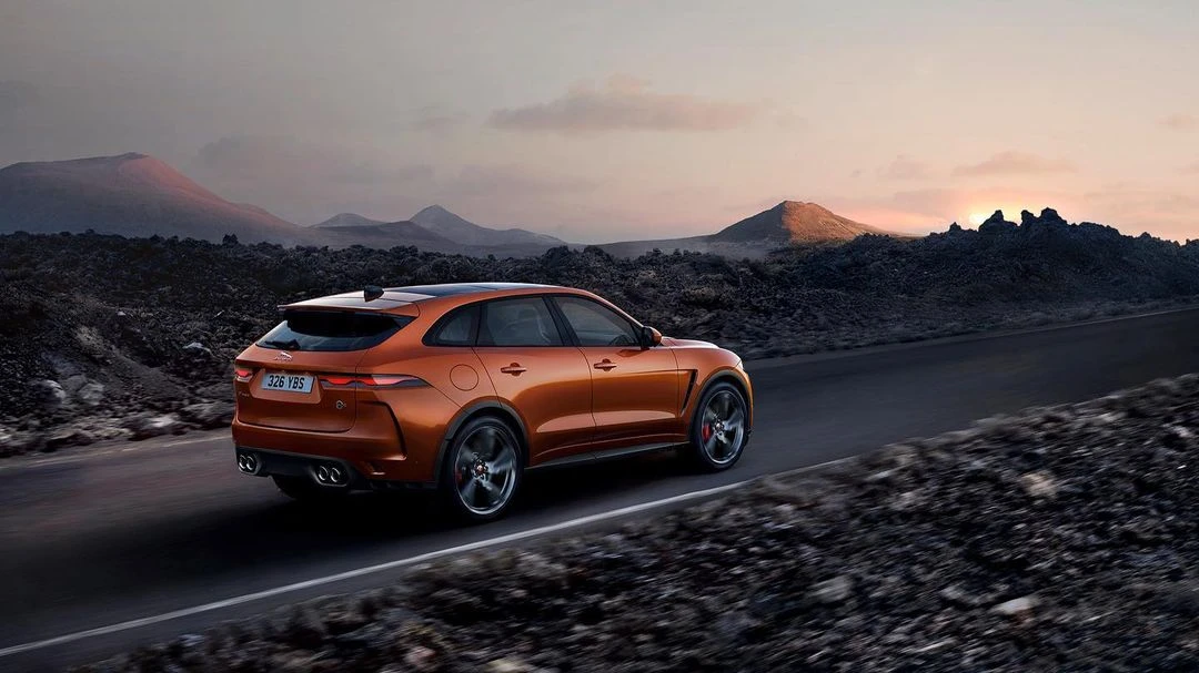 Copper-colored Jaguar F-Pace SVR driving on a desert road with distant mountains in the background at sunset. Automotive photography.