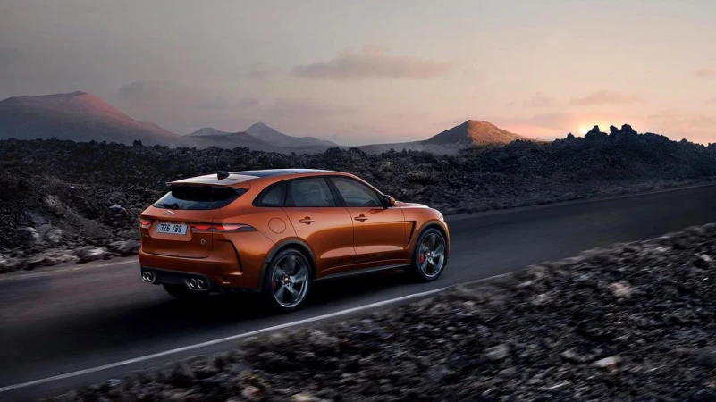 Copper-colored Jaguar F-Pace SVR driving on a desert road with distant mountains in the background at sunset. Automotive photography.
