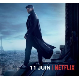 Omar Sy standing on a rooftop in a long dark coat and flat cap overlooking the Paris skyline at dusk.