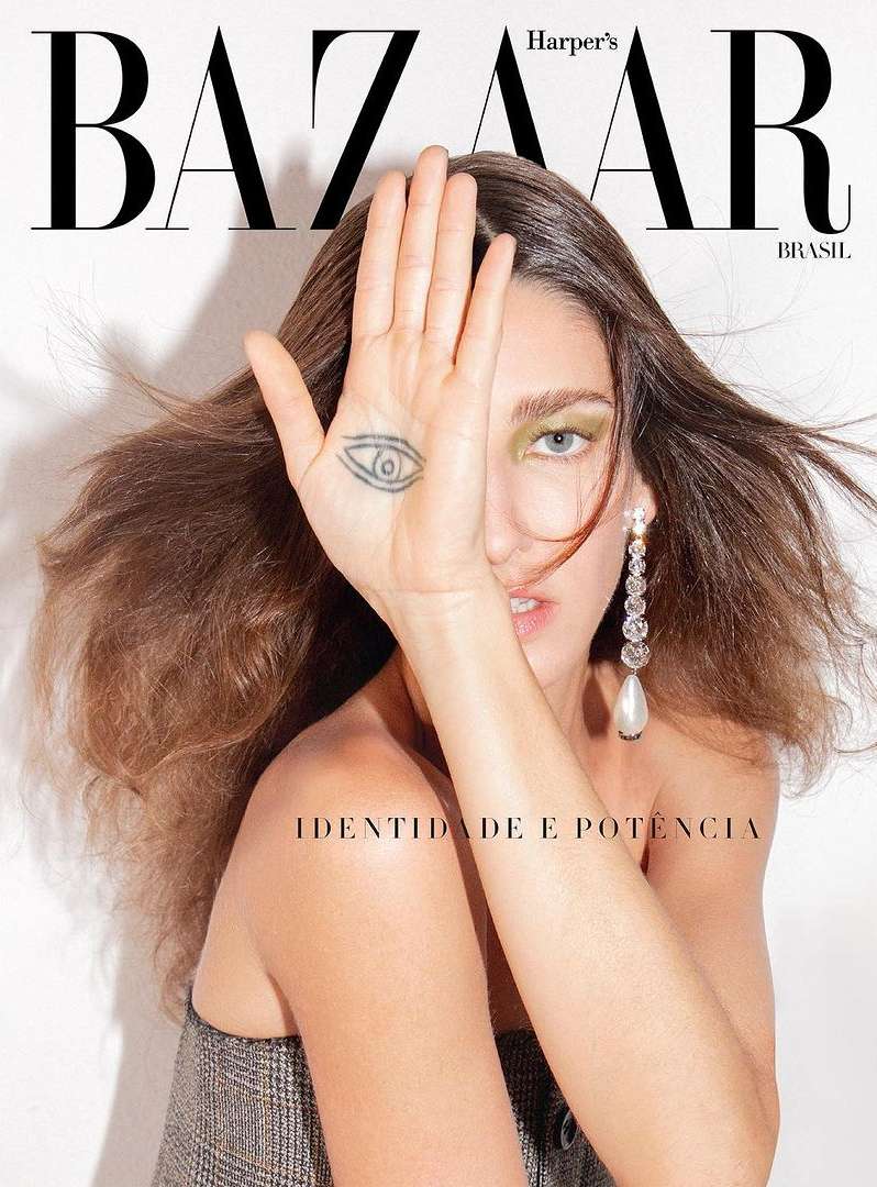 Fashion magazine cover featuring a woman with long brown hair, showcasing a hand tattoo and statement earrings against a white backdrop.