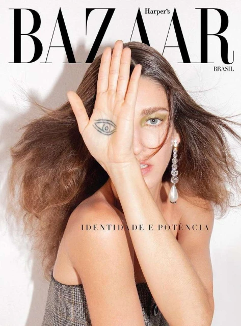 Fashion magazine cover featuring a woman with long brown hair, showcasing a hand tattoo and statement earrings against a white backdrop.