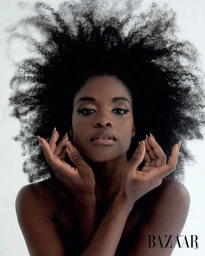 Close-up portrait of a Black woman with voluminous dark afro hair and manicured hands posed near her face.