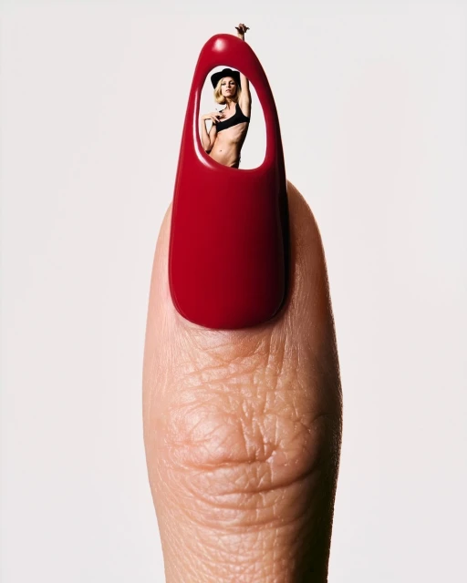 Woman with black hat and bikini top poses inside a red fingernail against a plain white background in a beauty and fashion composite image.