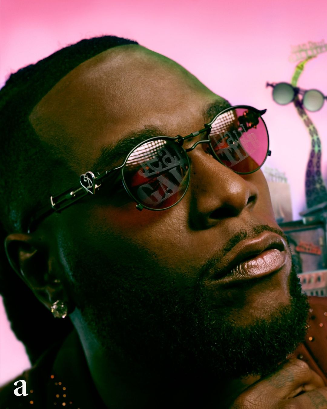 Close-up of adult male wearing sunglasses with reflected text in an urban-style setting with a pink gradient background.