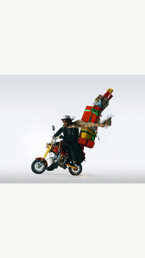 A person rides a motorcycle loaded with wrapped gifts against a neutral background, showcasing a festive and whimsical scene.