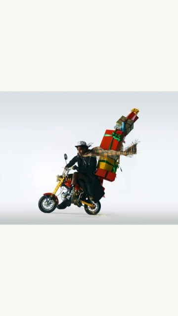 A person rides a motorcycle loaded with wrapped gifts against a neutral background, showcasing a festive and whimsical scene.