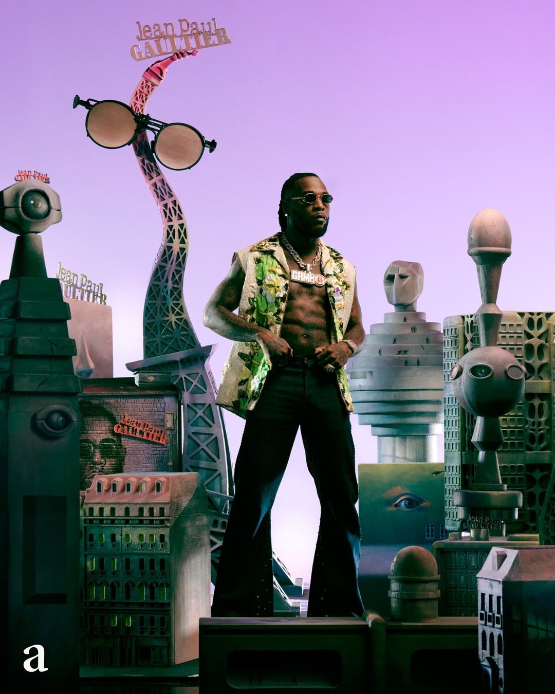 Adult male poses in a green vest, black pants, and jewelry amid surreal city backdrop with Eiffel Tower and Jean Paul Gaultier signage.