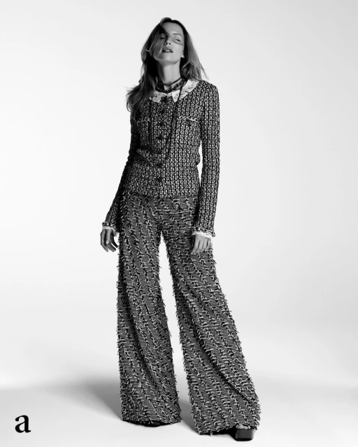 Black-and-white fashion portrait of a woman wearing a tweed jacket and wide-leg pants in a bright studio setting, stylish and elegant.