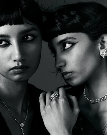 Close-up studio shot of two adult women wearing elegant jewelry and black clothing, striking dark eye makeup, and sleek dark bangs.