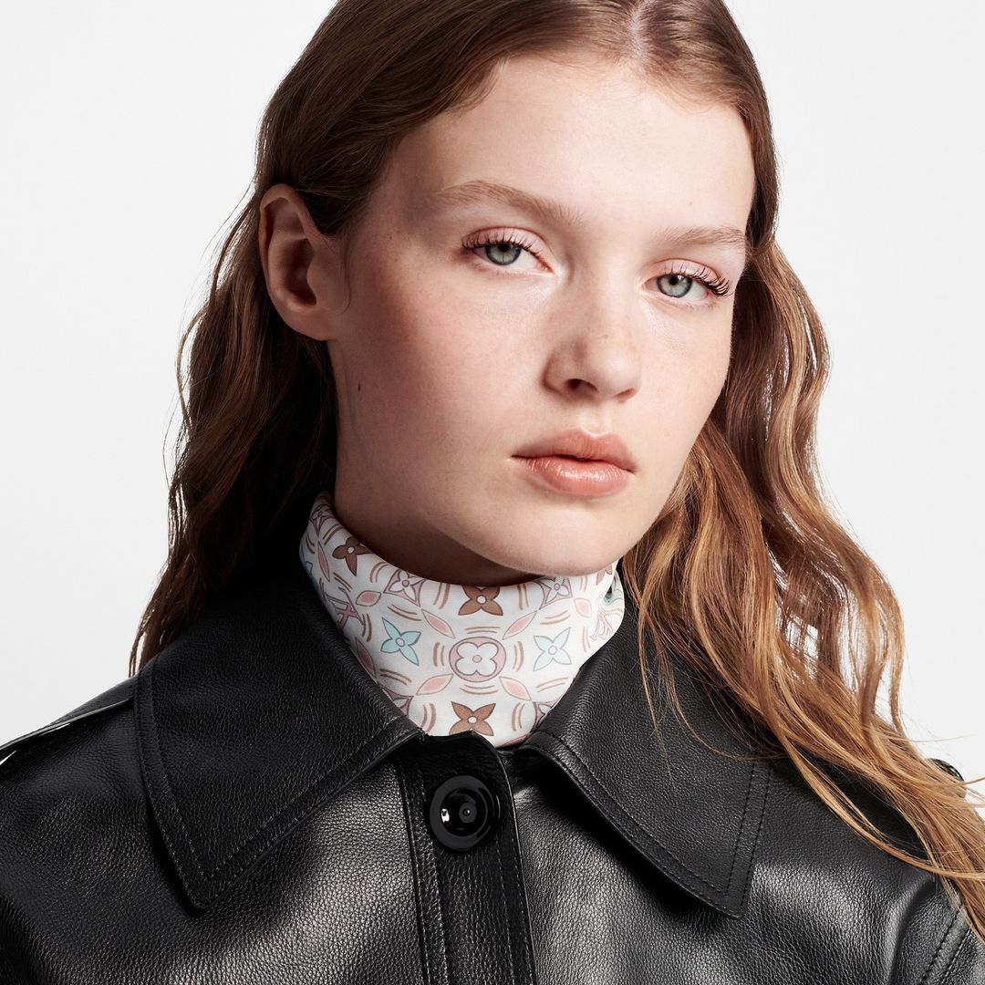 Portrait of a female model wearing a black leather jacket and a patterned silk neck scarf against a white background