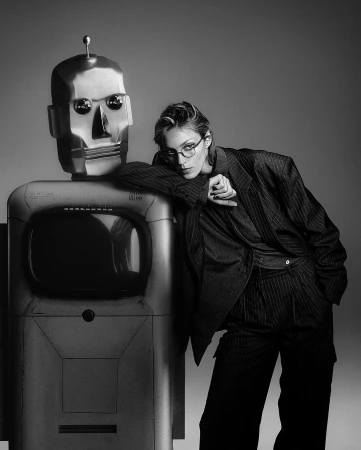 Monochrome fashion editorial portrait of a woman wearing pinstripe trousers and blazer leaning against a robot sculpture