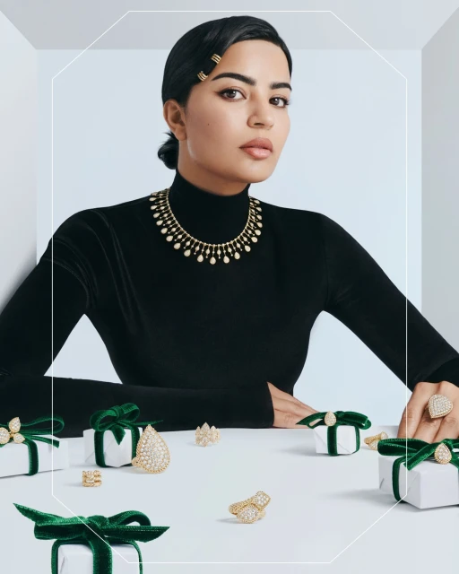 Woman in black turtleneck and jewelry posing with wrapped gifts on white surface, jewelry advertisement, indoor setting.