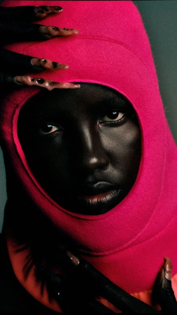 Close-up portrait of an African woman with painted nails and a pink hood, showcasing fashion and beauty against a blue background.