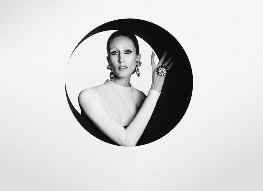 Striking black and white portrait of a woman with dramatic makeup, wearing a white top and bold jewelry, framed by a graphic black circle.