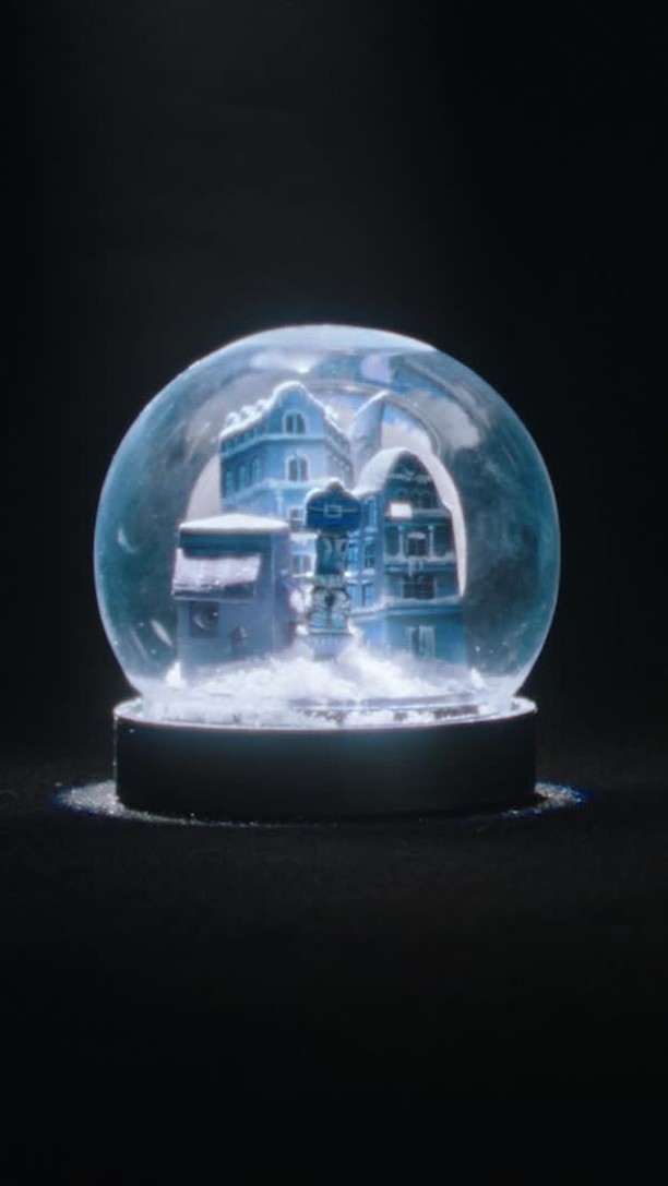 Snow globe featuring miniature buildings with snow on top, set against a dark background, creating a winter scene.