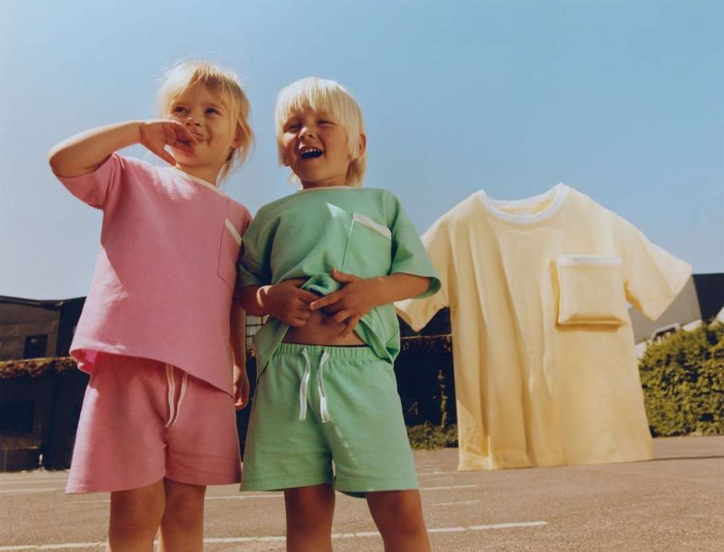 Two young children in matching pastel outfits stand outside with a third shirt in the background under a clear blue sky.