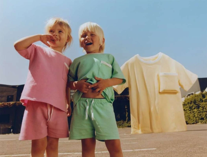 Two young children in matching pastel outfits stand outside with a third shirt in the background under a clear blue sky.